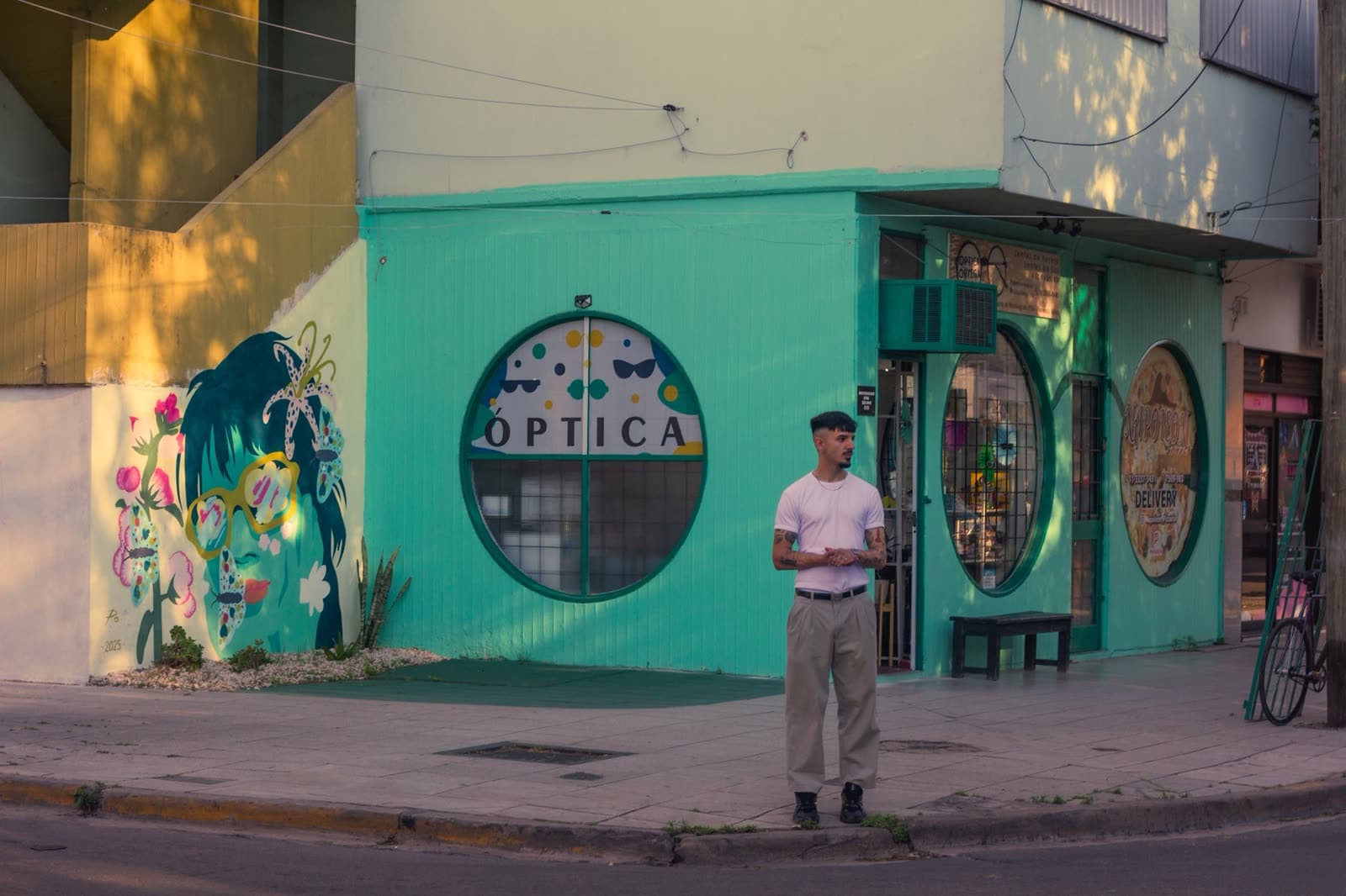 Esquina de una calle con un local pintado de verde y un mural en la pared