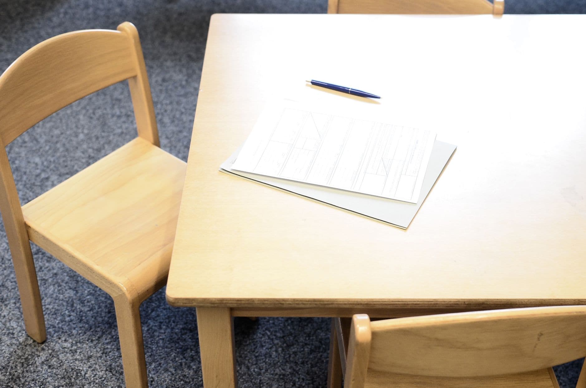 Mesa de reunión con sillas de madera, unos formularios y un bolígrafo
